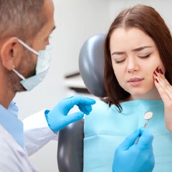 woman sitting in dental chair and holding her face in pain