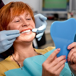 Older female patient examines smile in mirror