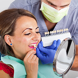 Woman comparing porcelain veneers to her natural teeth with dentist.