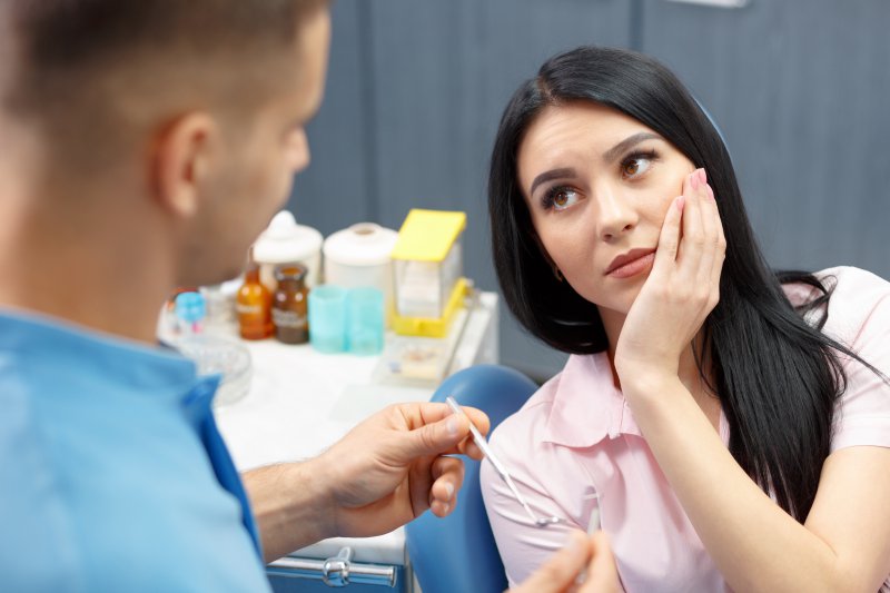 A woman holding her mouth while listening to a dentist.