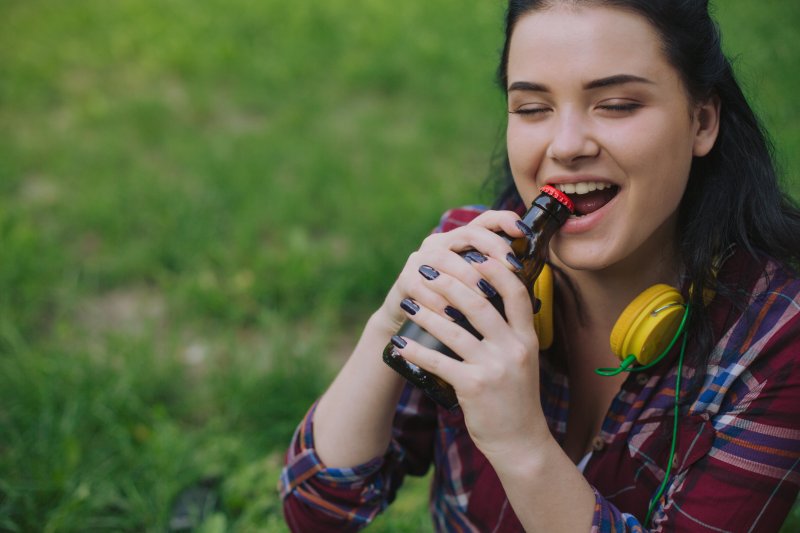 woman opening bottle with teeth