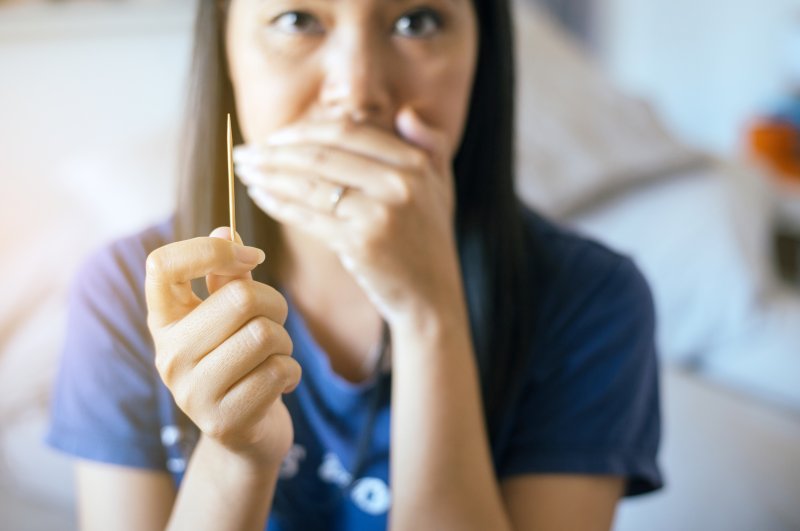 Person holding a toothpick and covering their mouth